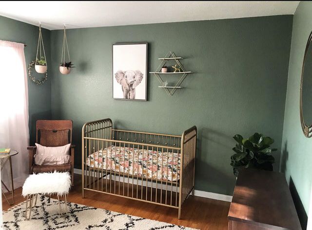 A nursery with sage green walls, a gold-painted crib, a wooden rocking chair, and a framed elephant print above the crib